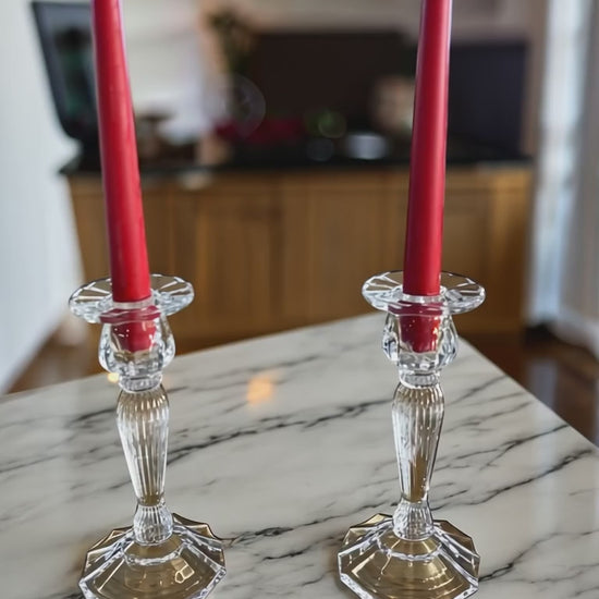 set of 2 red taper dinner candles in a glass candle holders on a white marble worktop with the kitchen in the background