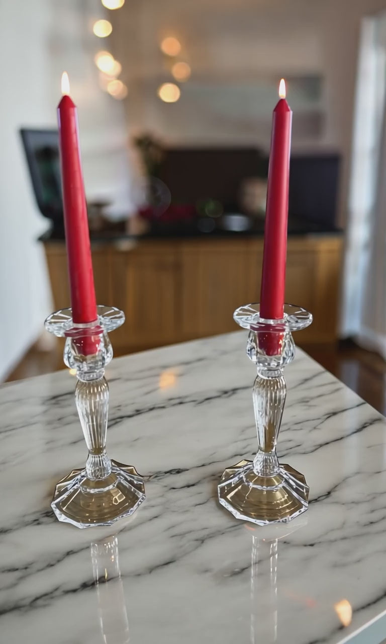 set of 2 red taper dinner candles in a glass candle holders on a white marble worktop with the kitchen in the background